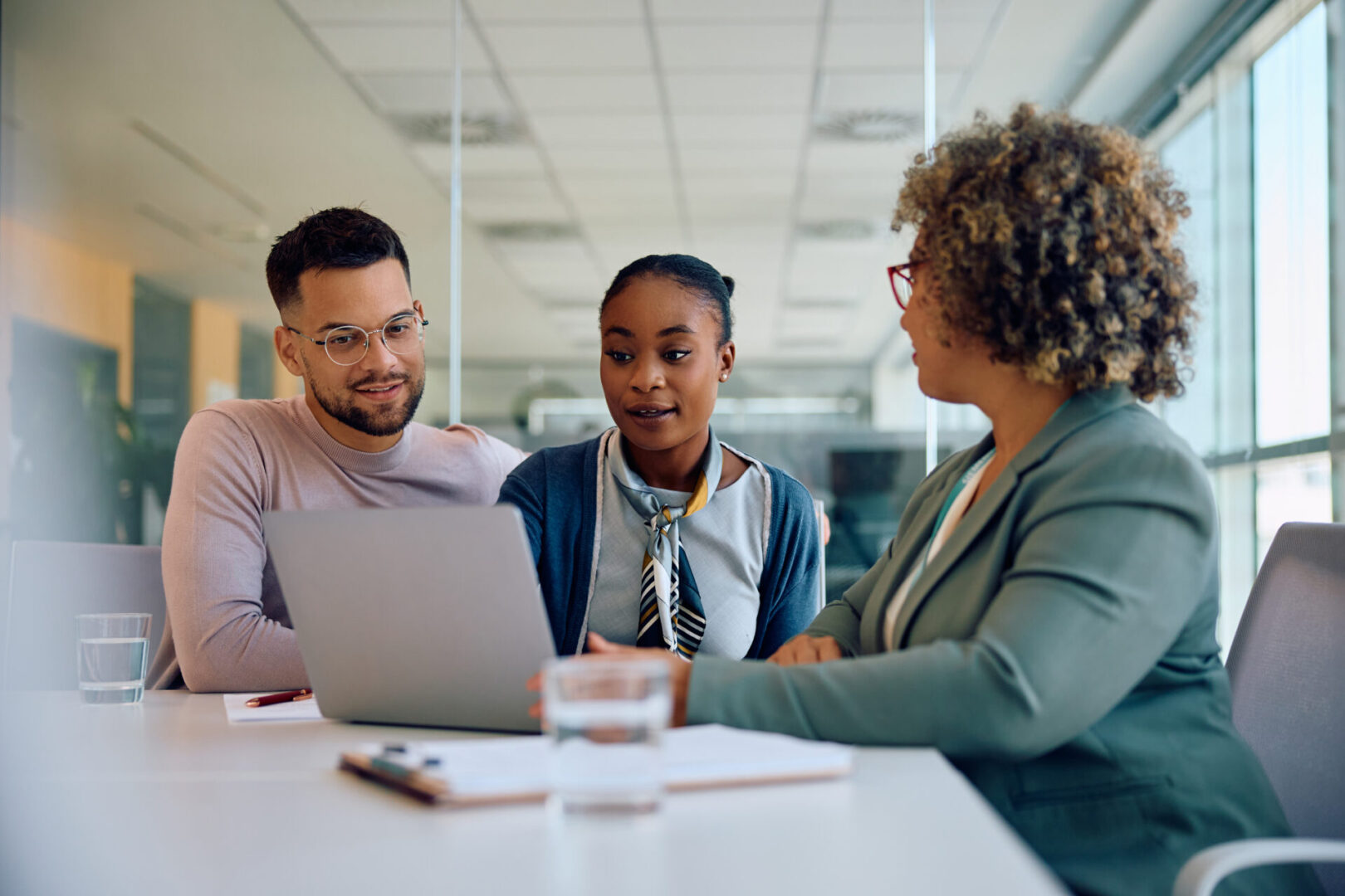 Young couple and their financial advisor using laptop during a meeting in the office. Three people discussing around a laptop.